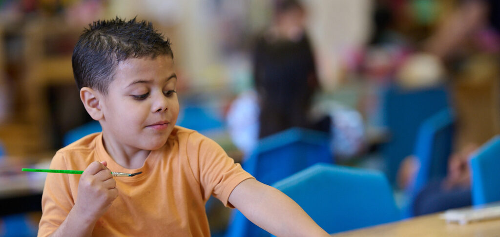 Child playing in a classroom with a focused expression while seated at a table.
