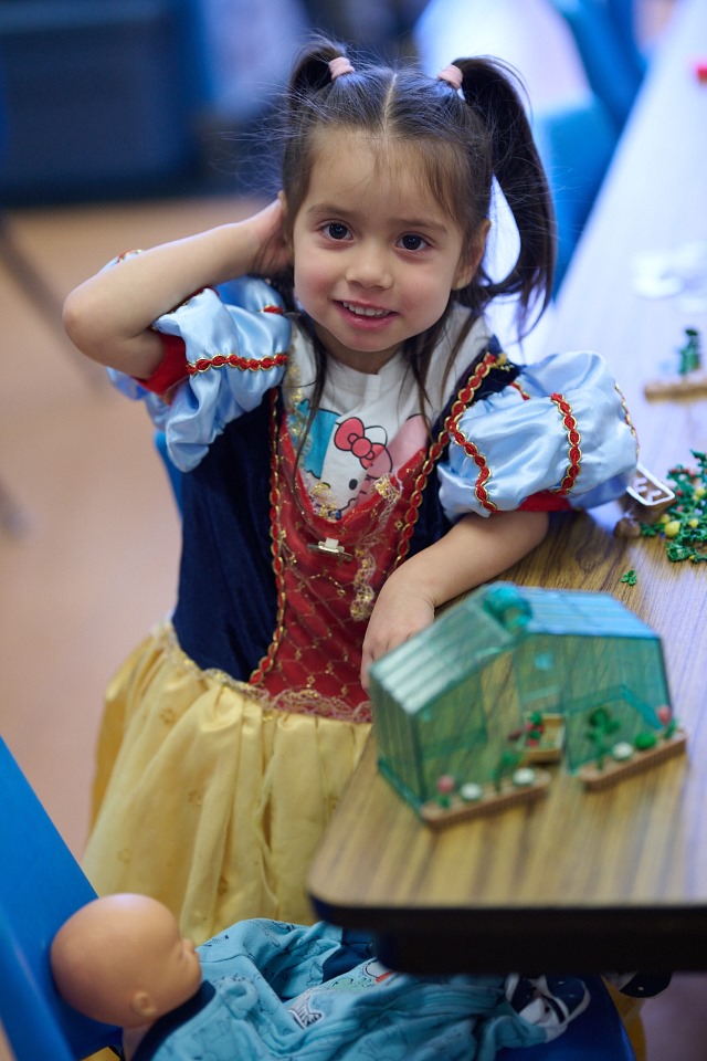 Child in a Snow White costume smiling, standing by a table with a model greenhouse.