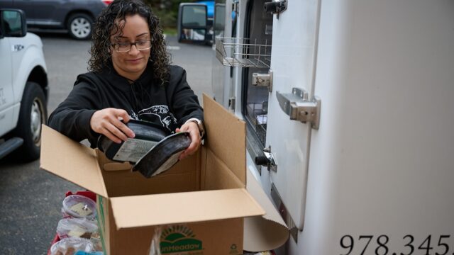 Person placing a small appliance into a cardboard box near a delivery truck.