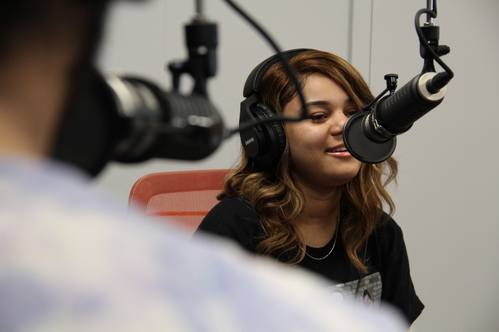 Person speaking into a microphone in a recording studio, wearing headphones.