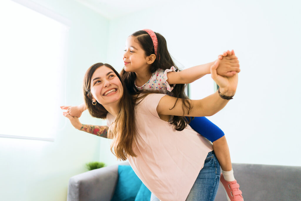 Mother and daughter playing and smiling indoors on a sofa soft lighting and colorful decor in the background