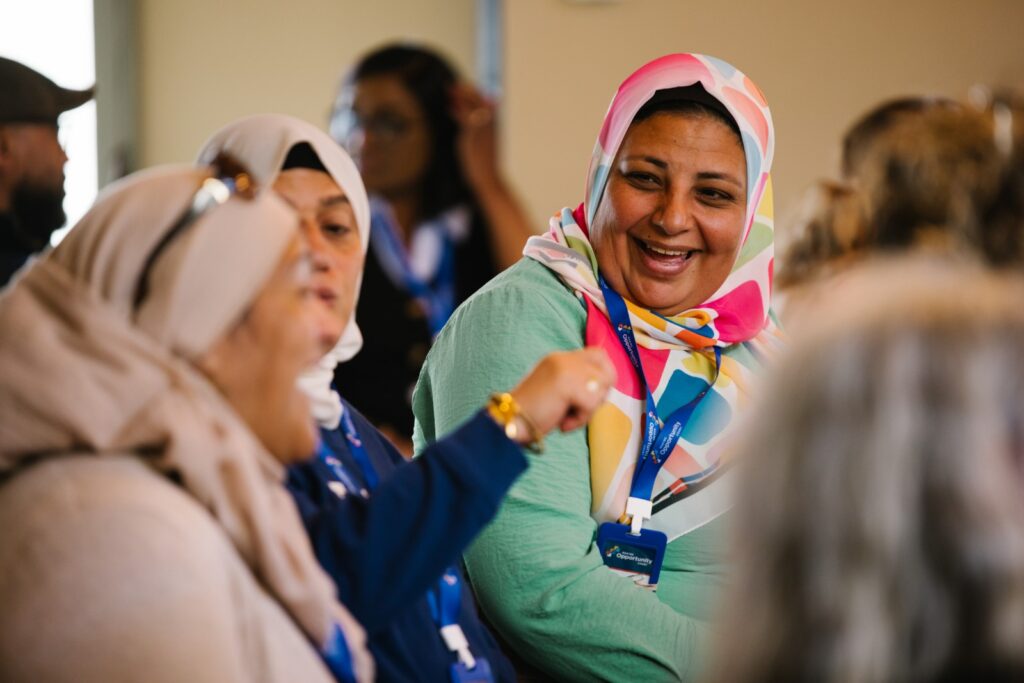 Women sitting together, smiling and engaging in conversation at a community event.