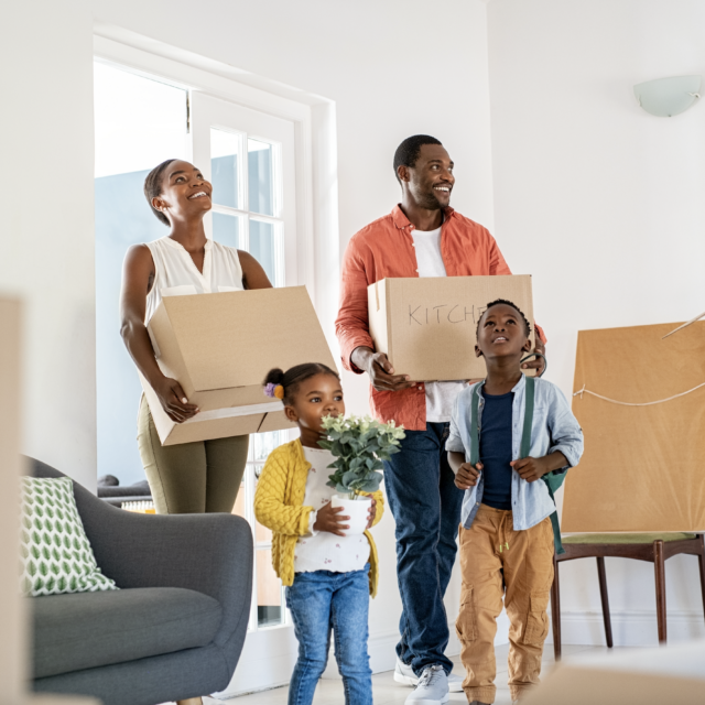 Family carrying boxes into new home, smiling and looking excited.