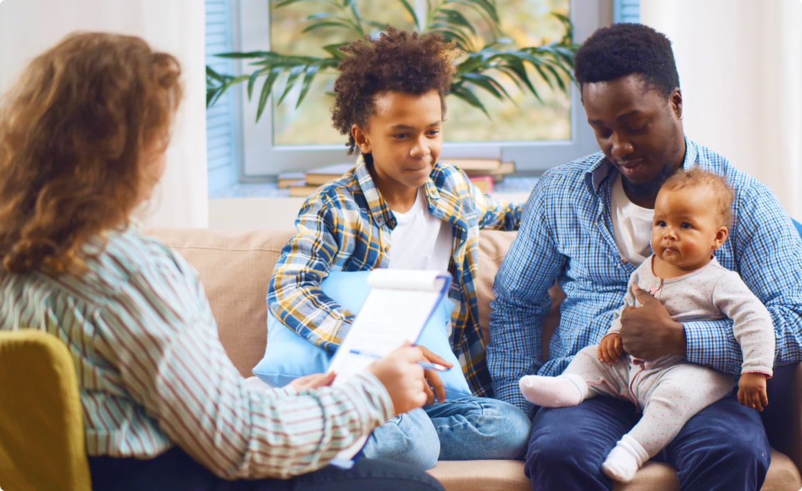 Family with two children sitting on a couch during a counseling session with a therapist in a cozy living room.