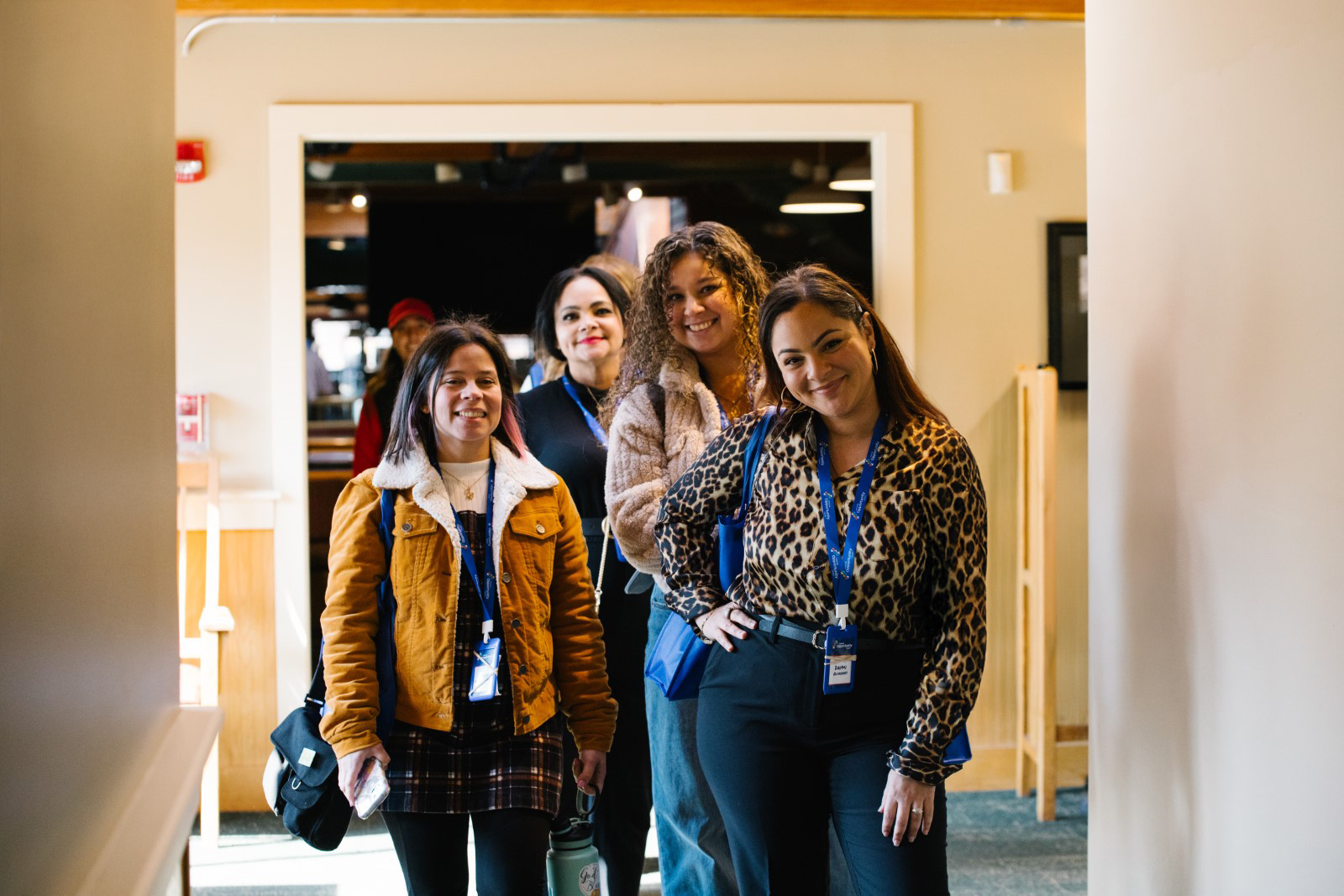 Group of four women smiling and wearing conference lanyards inside a warmly lit room
