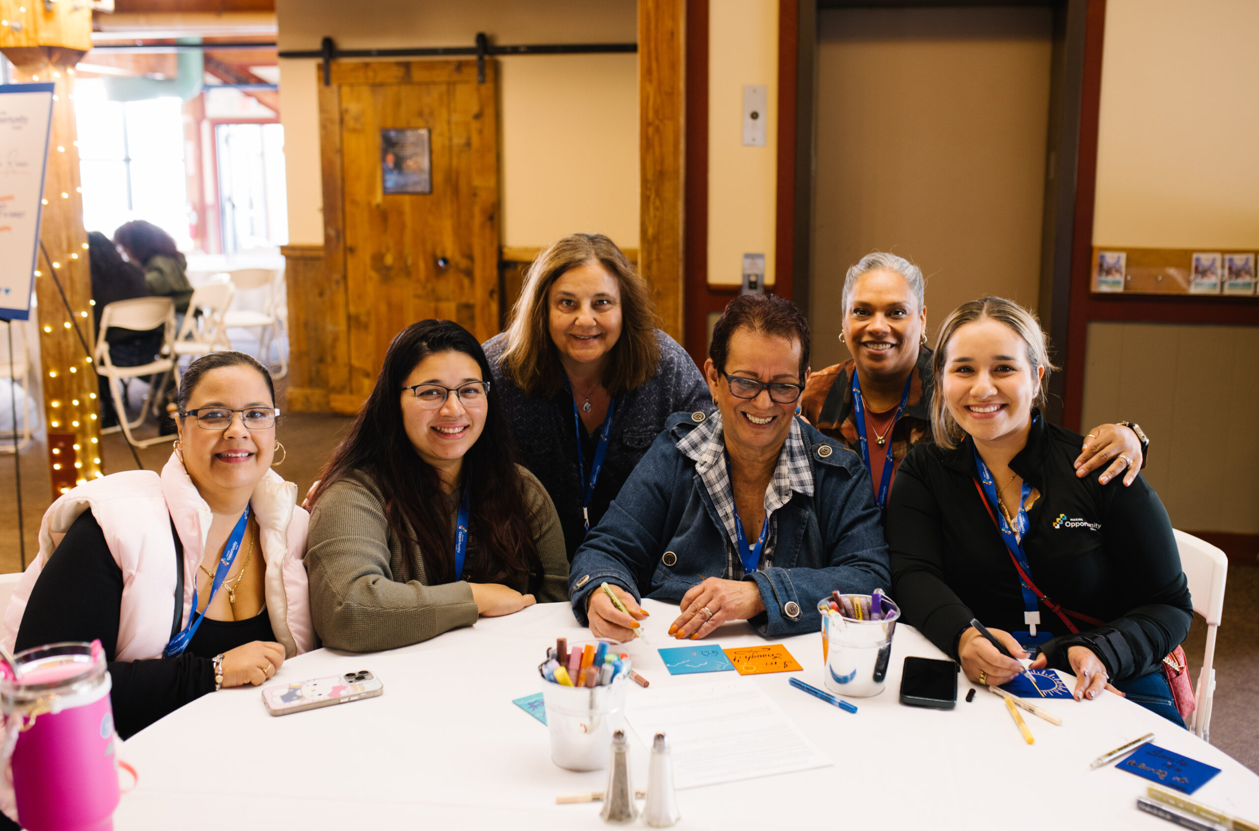 Group of six people smiling around a table with crafts and art supplies in a cozy indoor setting.