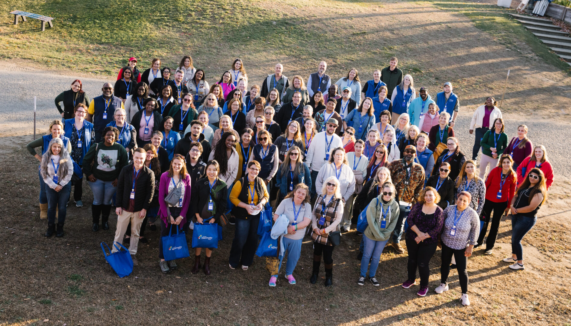 Group of people standing outside, smiling at the camera, with grass and stairs in the background.