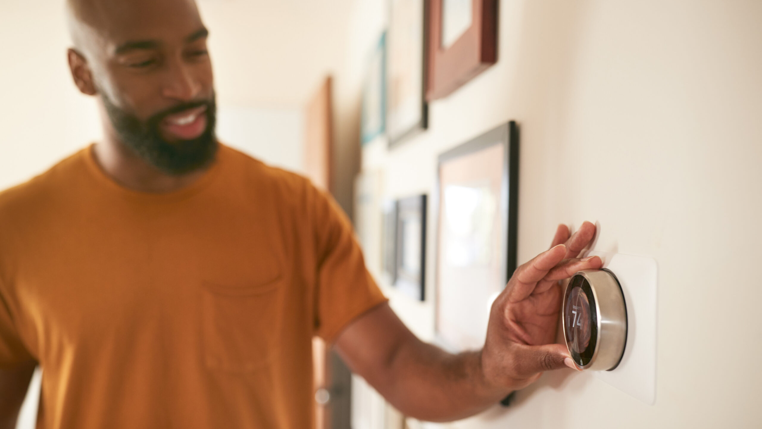 Person smiling and adjusting a digital thermostat on a wall in a warmly lit room.