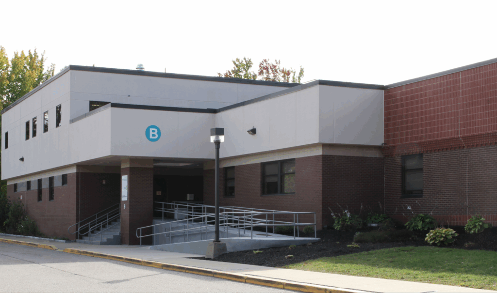 Front view of a school building entrance with accessible ramps and a sign labeled B on a sunny day.