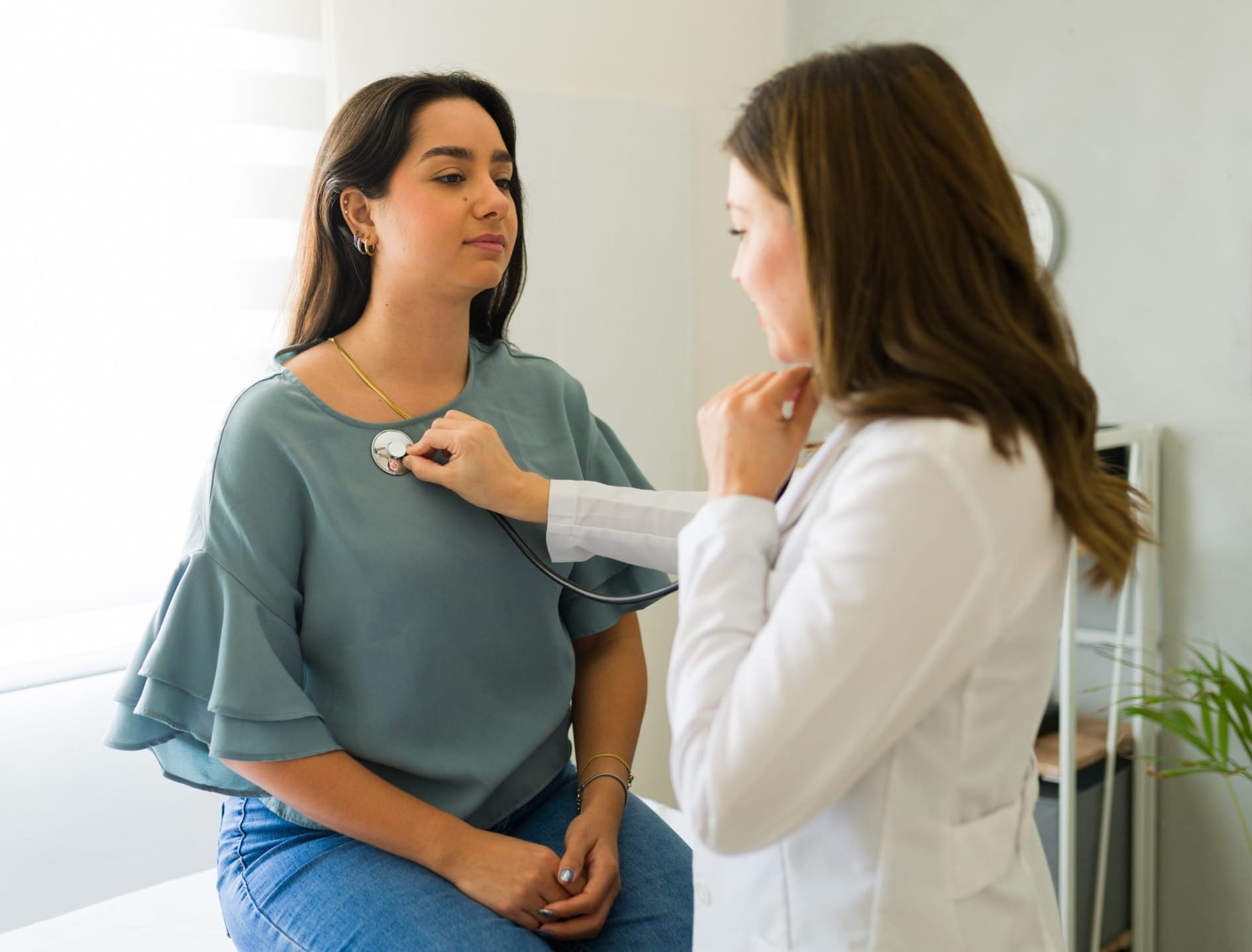 Doctor using stethoscope to listen to a patient's chest during a medical examination in a clinic.