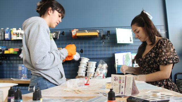 Two people crafting with resin at a work table, with art supplies and materials in the background.