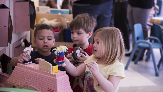 Children playing with dolls in a classroom setting, exploring a toy house together.