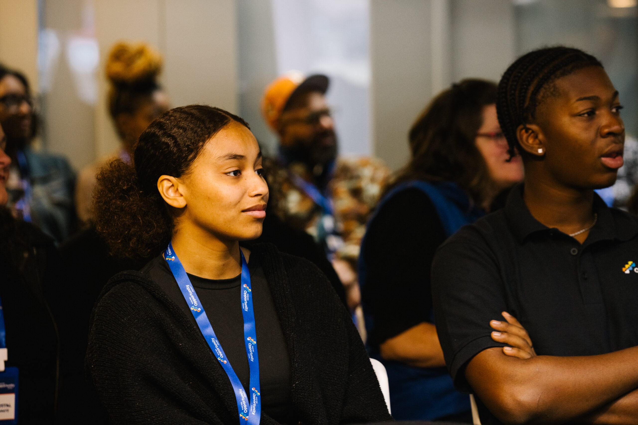 People sitting attentively in a conference room, wearing lanyards and engaged in a presentation.