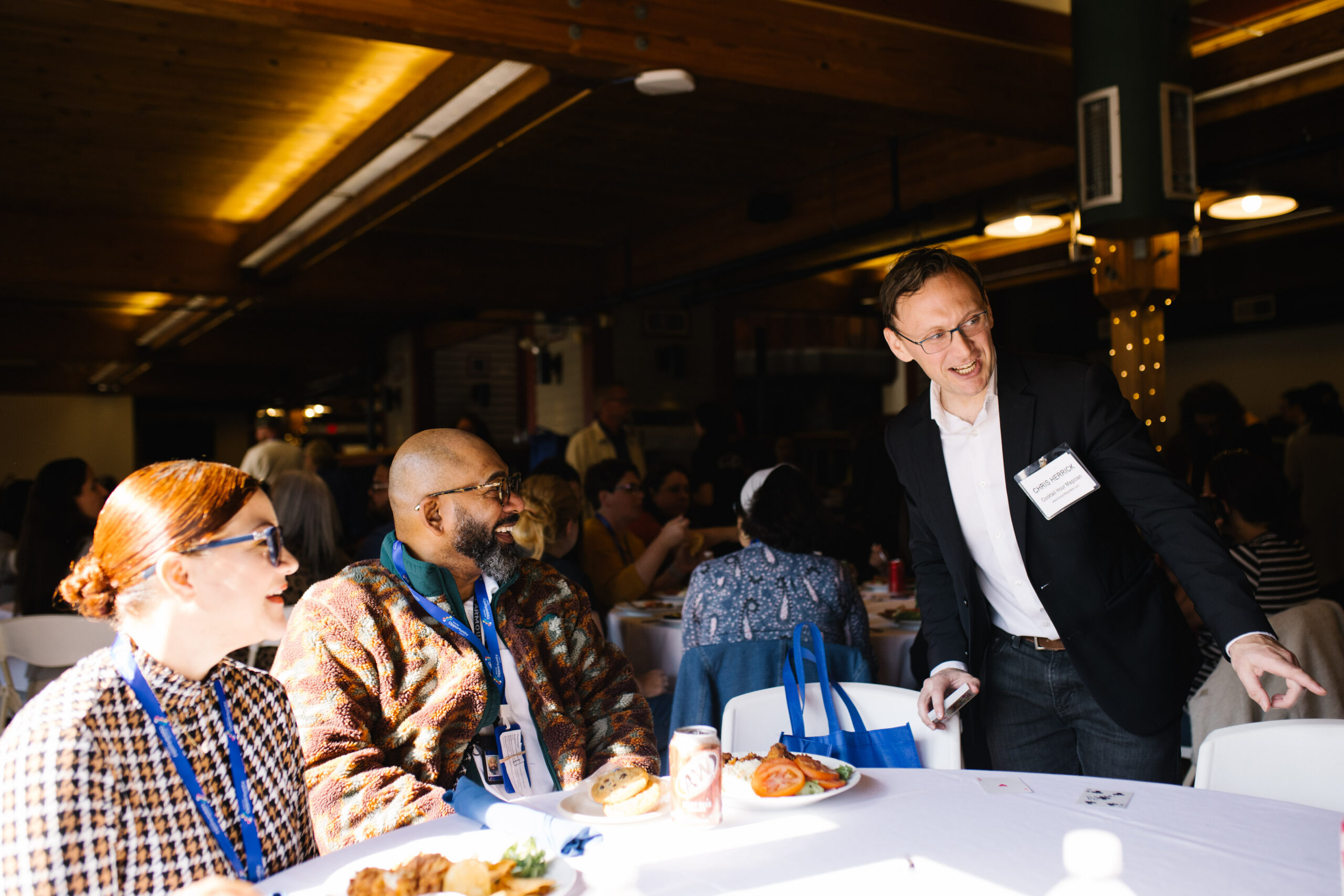 People seated at a table enjoying a meal and conversation in a warmly lit event space.
