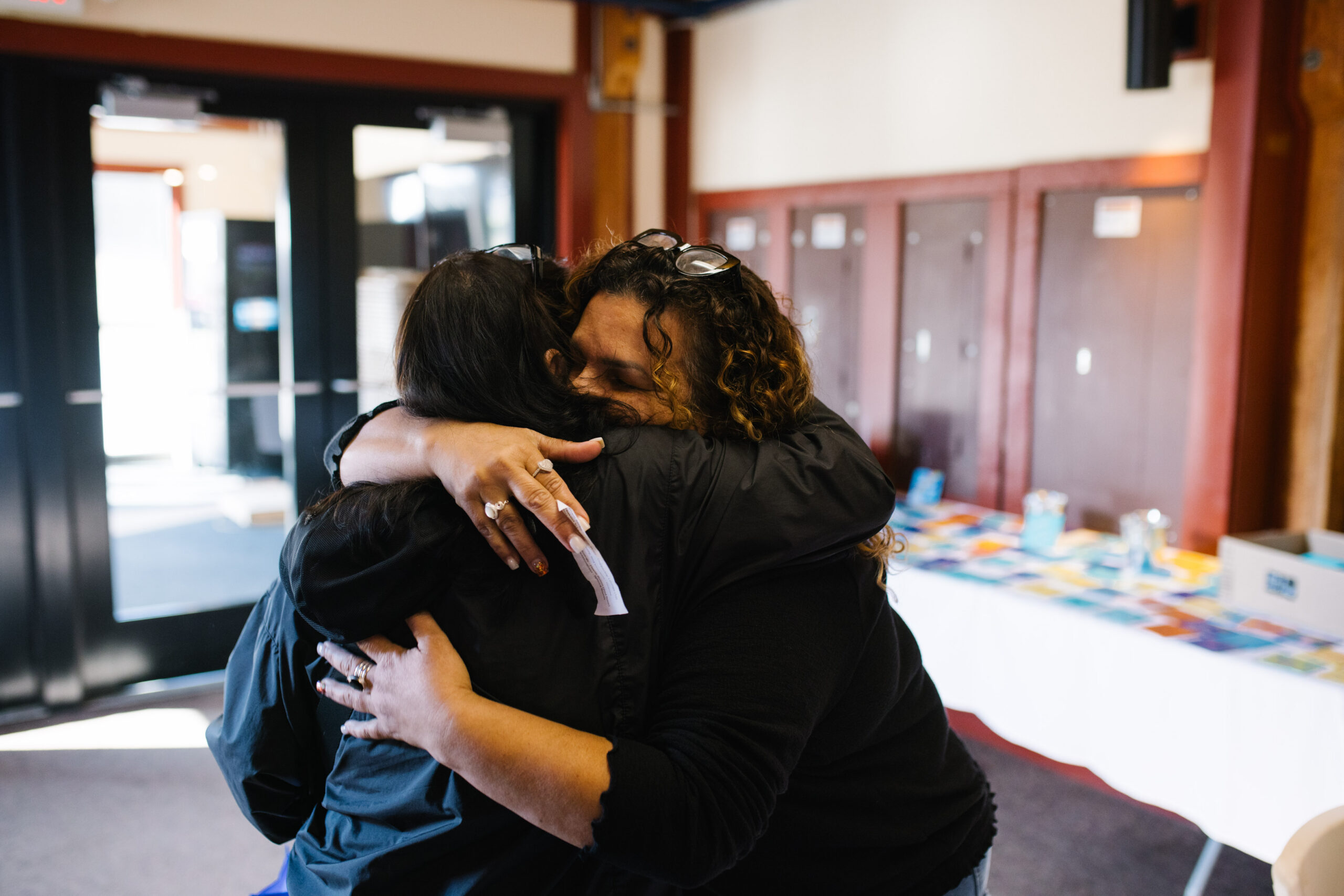 Two people embracing warmly inside a building with tables in the background.