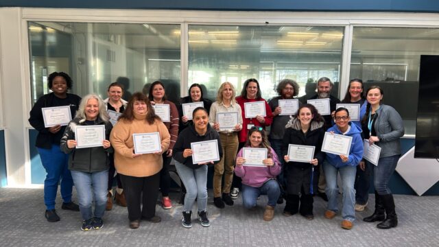 Group of people smiling and holding certificates in an office setting.
