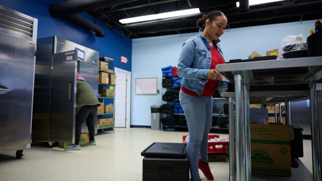 Two people organizing boxes and supplies in a storage room with blue walls and industrial shelving.