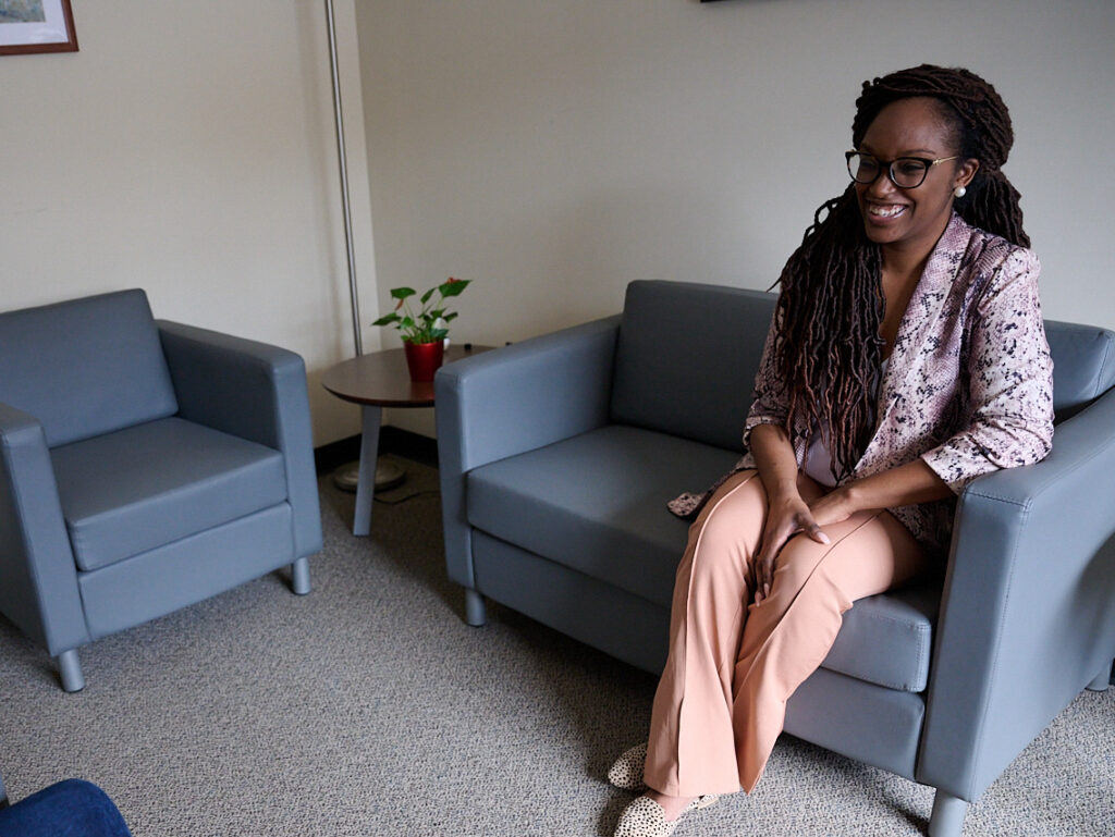 Person sitting on a gray sofa in a well-lit room with a small plant on a table.